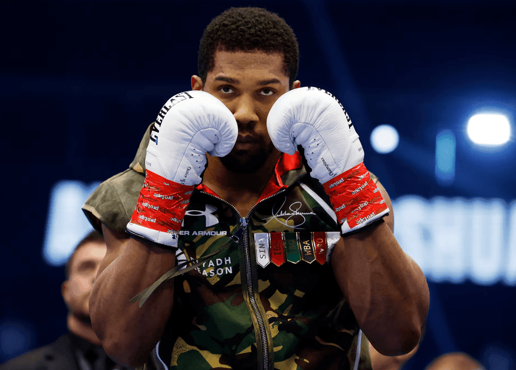 Anthony Joshua với vẻ mặt quyết tâm, mặc áo khoác rằn ri và găng tay trắng, chuẩn bị cho trận đấu trở lại sau bi kịch cá nhân.