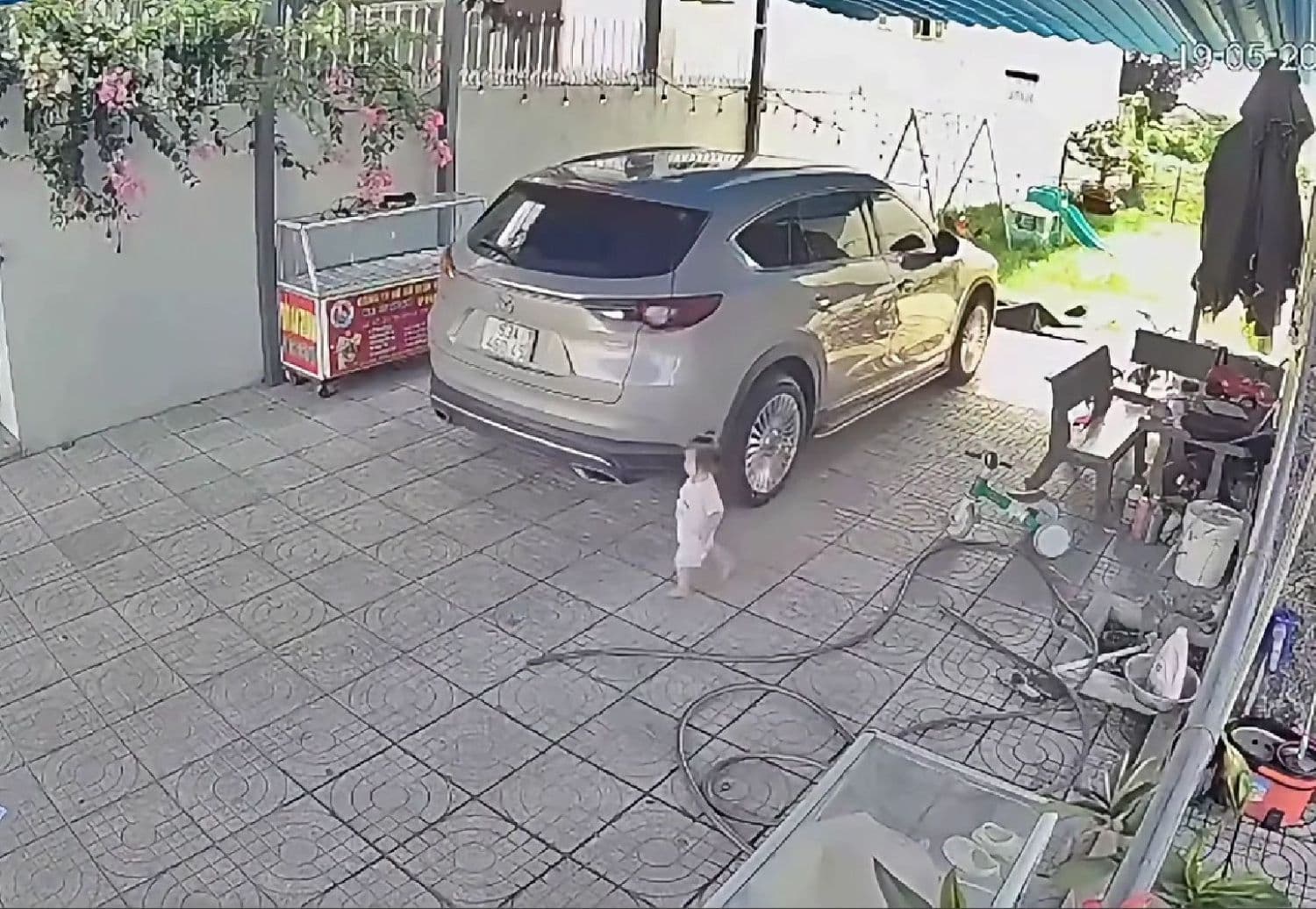 Bé gái 15 tháng tuổi đi bộ phía sau ô tô đang lùi trong sân nhà, minh họa nguy hiểm từ điểm mù xe.