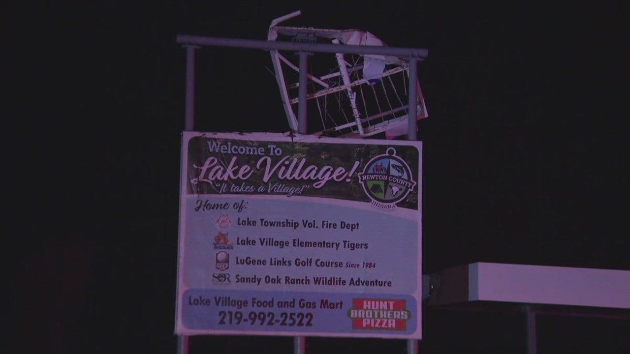 Biển hiệu "Welcome to Lake Village!" bị hư hại nặng, tượng trưng cho sự mong manh của hạ tầng đô thị trước thiên tai.