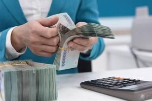 Bàn tay đang đếm tiền Việt Nam đồng bên cạnh máy tính, tượng trưng cho việc tính toán lương tối thiểu.