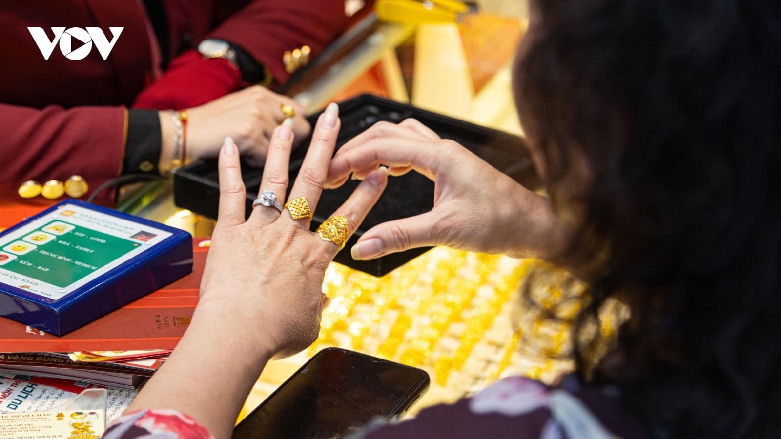 Bàn tay đeo nhẫn vàng đang xem xét sản phẩm vàng, minh họa tâm lý đầu tư cá nhân và quyết định mua vàng.