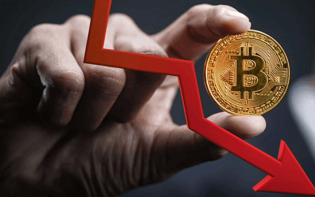 Bàn tay giữ đồng Bitcoin vàng với mũi tên đỏ đi xuống, minh họa sự biến động giá và tác động của chính sách tiền tệ