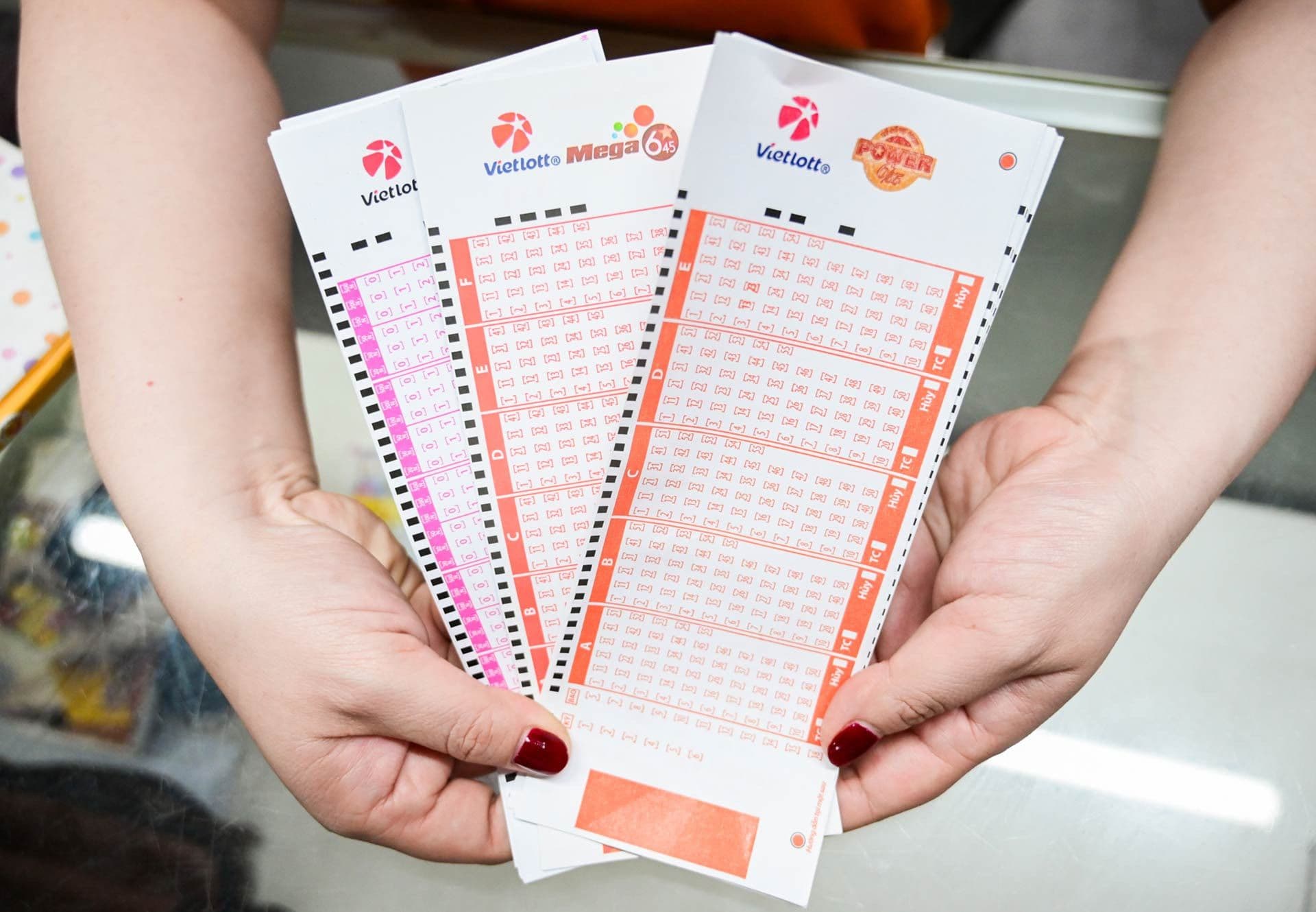 Bàn tay người chơi cầm nhiều vé số Vietlott Mega 6/45 và Power 6/55.