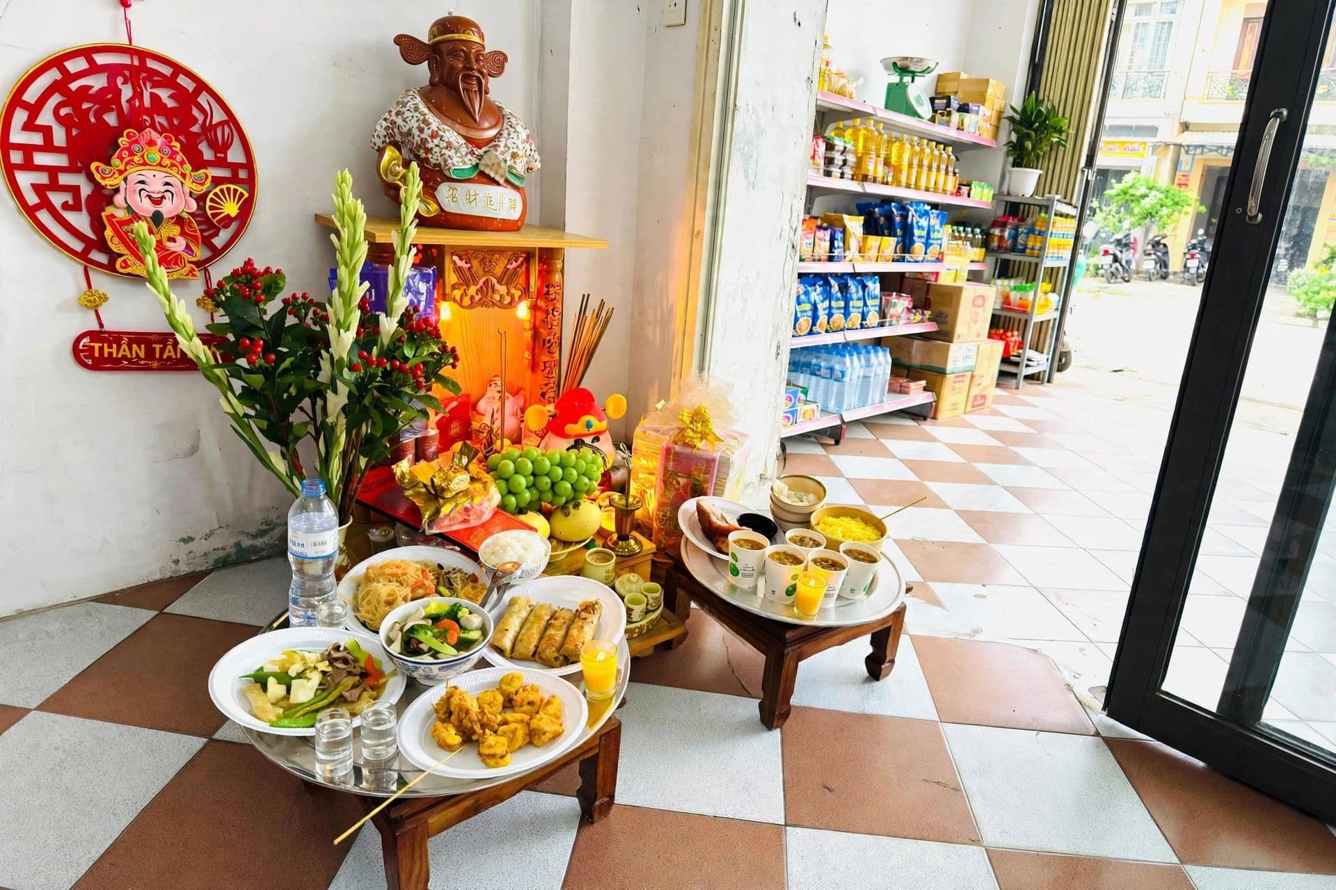 Bàn thờ Thần Tài với các lễ vật truyền thống trong một cửa hàng nhỏ, tượng trưng cho nghi lễ tâm linh đang thích nghi với bối cảnh hiện đại.