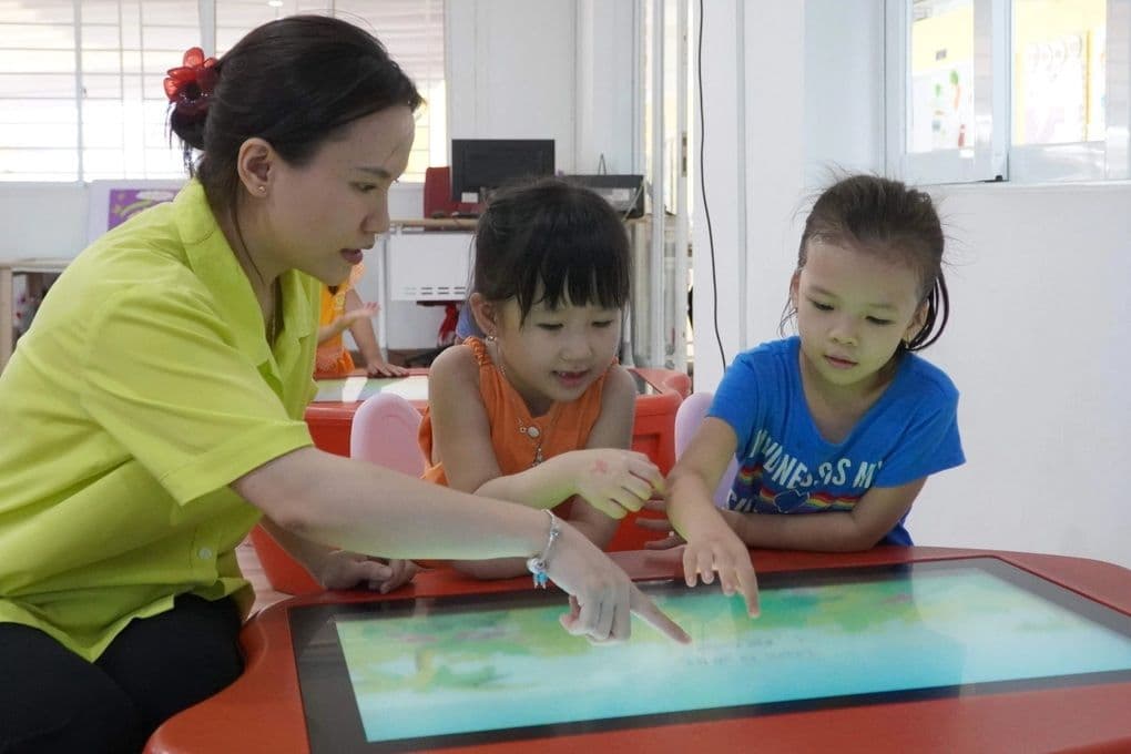 Cô giáo mầm non hướng dẫn trẻ em học trên bàn tương tác kỹ thuật số