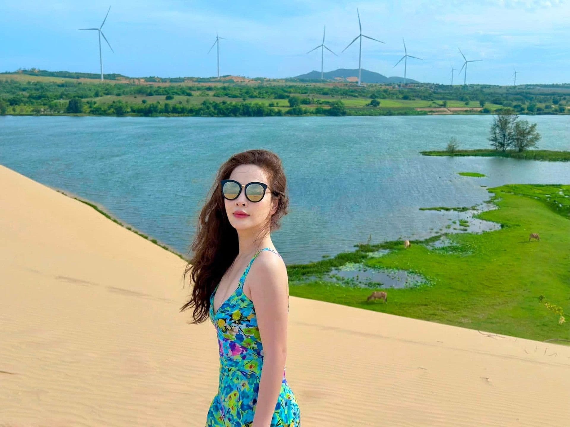 Ca sĩ Hòa Minzy tạo dáng trên đồi cát với trang phục sặc sỡ, thể hiện hình ảnh người nổi tiếng trong không gian công cộng và hành trình cảm xúc công khai.