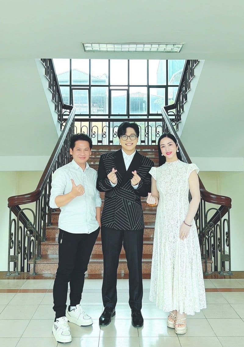 Ca sĩ Đàm Vĩnh Hưng lịch lãm trong bộ vest sọc, tạo dáng cùng hai người khác, thể hiện hình ảnh 'Ông hoàng nhạc Việt' trên sân khấu.