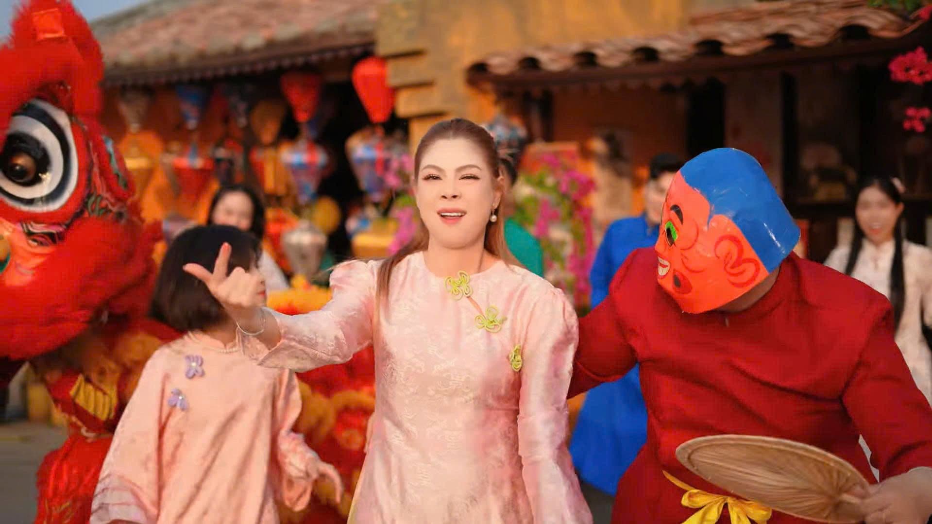 Ca sĩ Thanh Thảo biểu diễn nhạc Tết trong trang phục truyền thống màu hồng nhạt, xung quanh là các vũ công múa lân, thể hiện không khí lễ hội và sự trở lại của nghệ sĩ gạo cội.