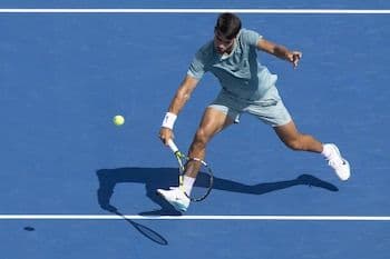 Carlos Alcaraz đang thực hiện cú đánh mạnh mẽ trên sân quần vợt xanh, thể hiện sự quyết tâm và bản lĩnh.