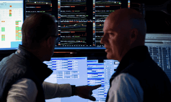 Các chuyên gia tài chính phân tích dữ liệu trên nhiều màn hình, thể hiện việc tối ưu hóa vận hành và quản lý chuỗi cung ứng.