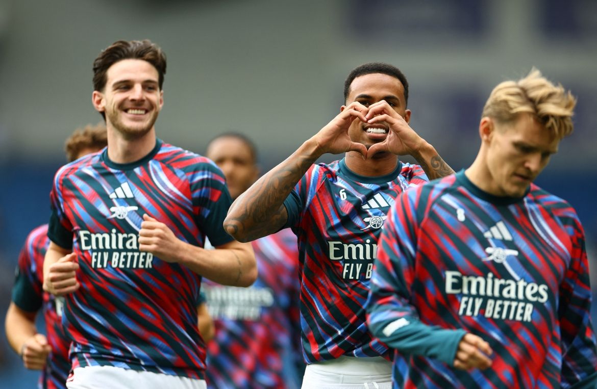 Các cầu thủ Arsenal vui vẻ trên sân, một cầu thủ tạo hình trái tim bằng tay, tượng trưng cho tinh thần cộng đồng và niềm đam mê bóng đá.