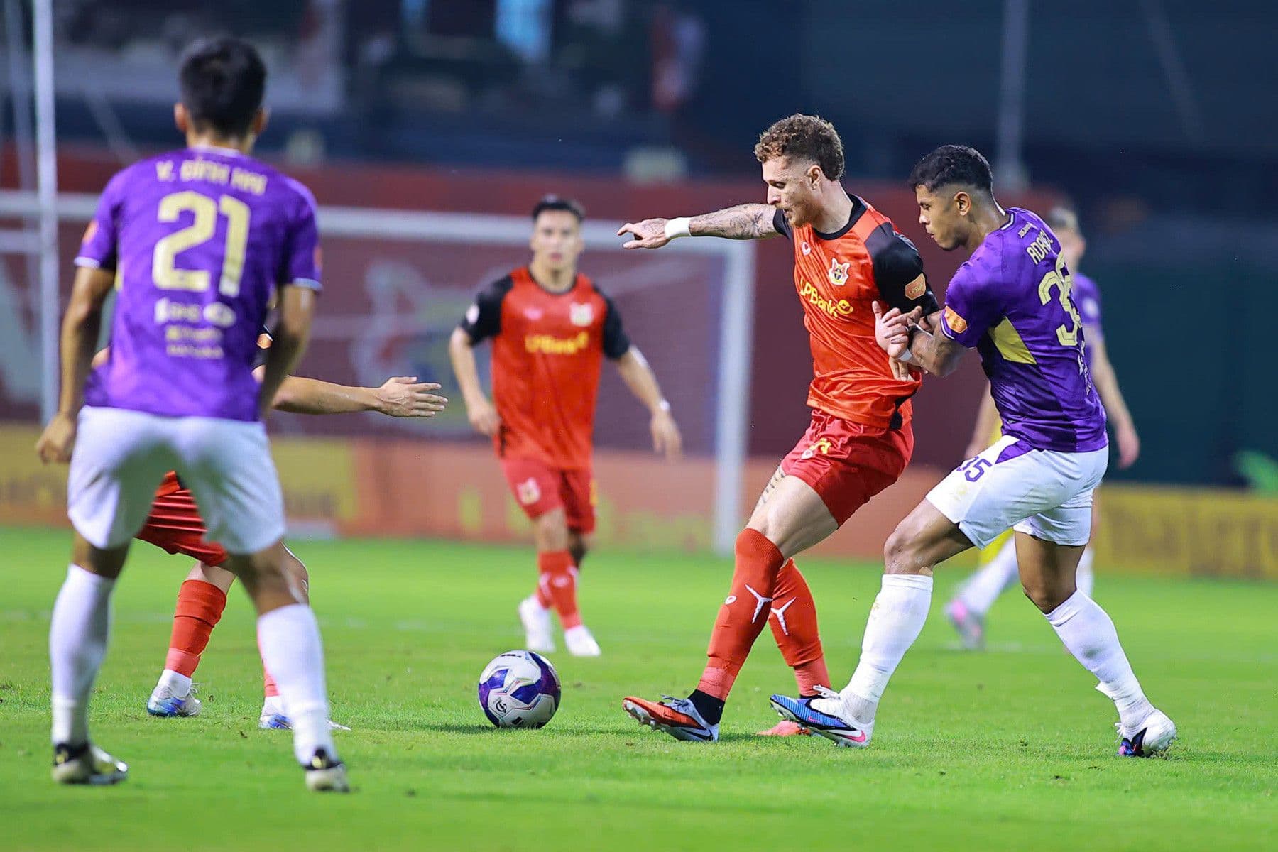 Các cầu thủ Ninh Bình FC và Hà Nội FC tranh tài trên sân, thể hiện sự đối lập trong triết lý bóng đá giữa các câu lạc bộ V-League.