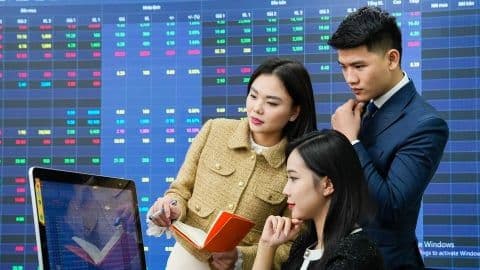 Các doanh nhân trẻ thảo luận chiến lược kinh doanh trước màn hình hiển thị dữ liệu tài chính, tượng trưng cho tư duy quản trị chuyên nghiệp.