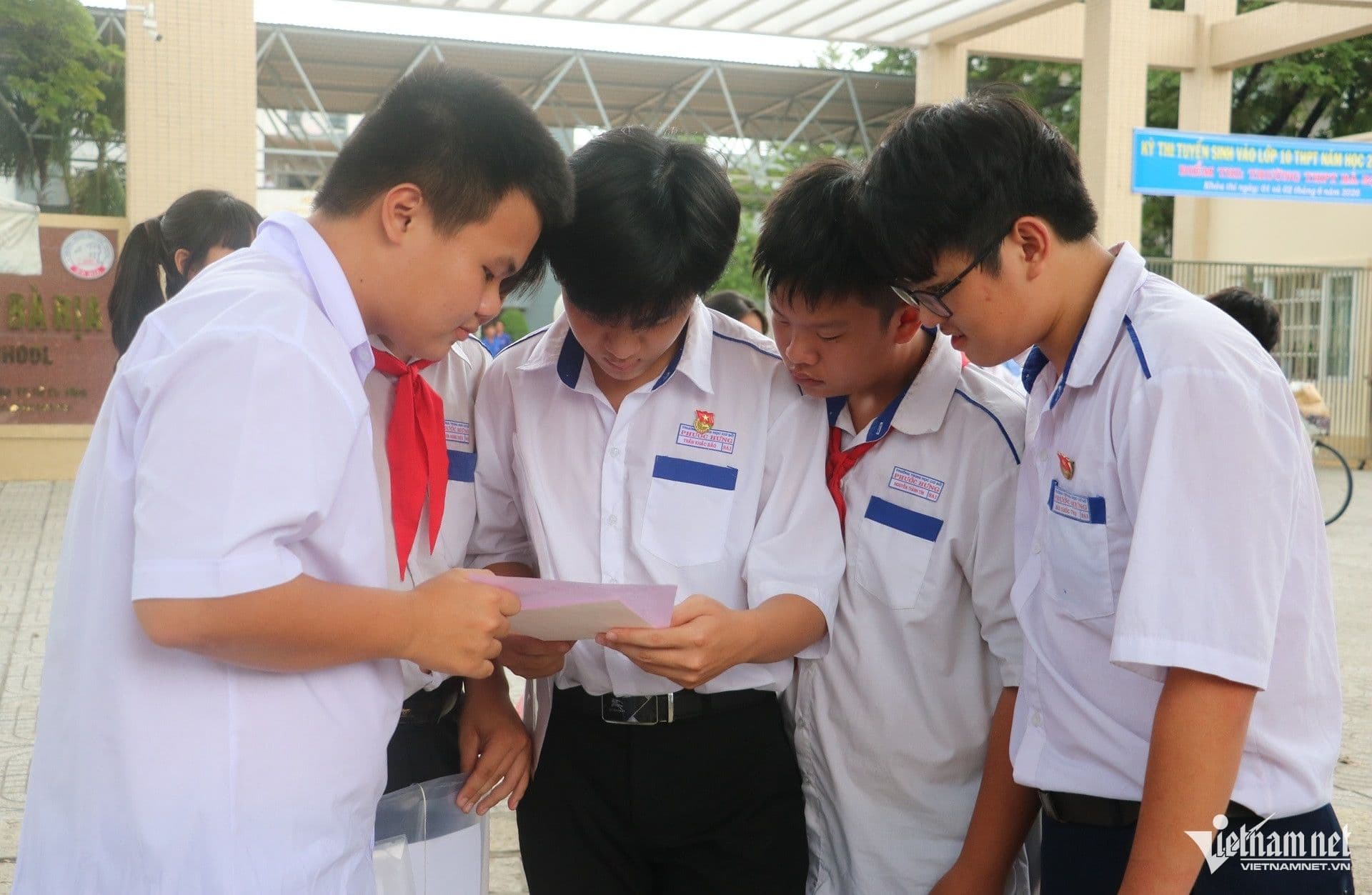 Các thí sinh nam tập trung xem xét một đề thi hoặc tài liệu, thảo luận về độ khó của bài thi Tiếng Anh lớp 10.