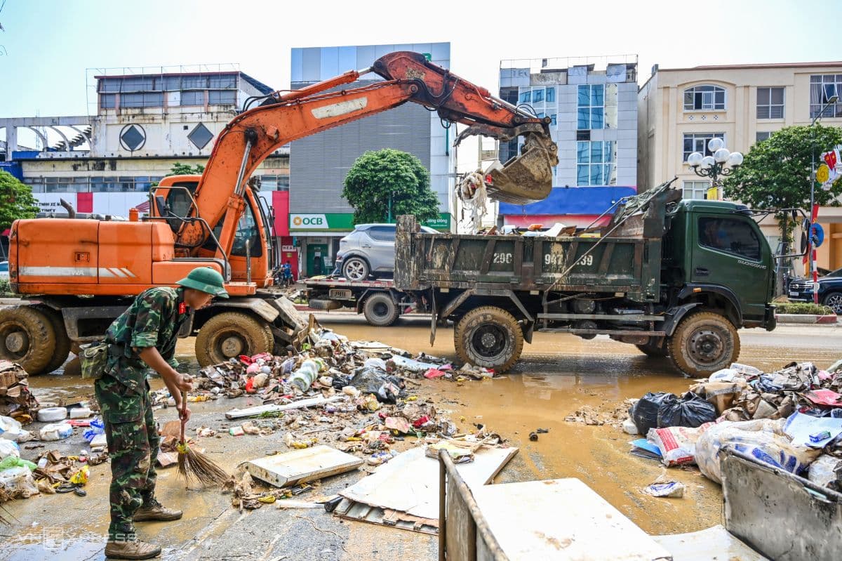 Cán bộ, chiến sĩ và máy xúc cùng nhau dọn dẹp bùn đất, rác thải trên đường phố sau lũ.