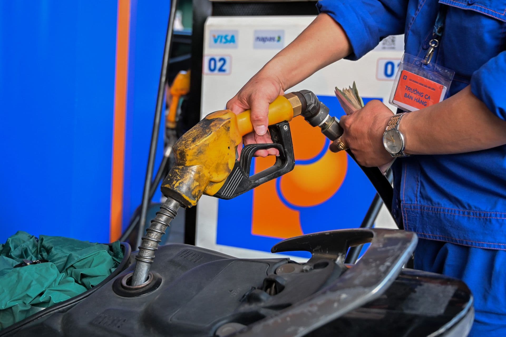 Cận cảnh vòi bơm xăng và tay người đổ xăng, biểu thị chi phí xăng dầu cho người dân.