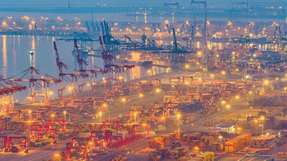 Cảng biển với nhiều container và cần cẩu, thể hiện sự năng động của thương mại và chuỗi cung ứng toàn cầu.