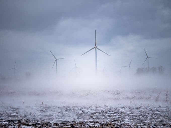 Cánh đồng với tua bin gió trong sương mù dày đặc, thể hiện không khí lạnh giá và mờ ảo của mùa đông.