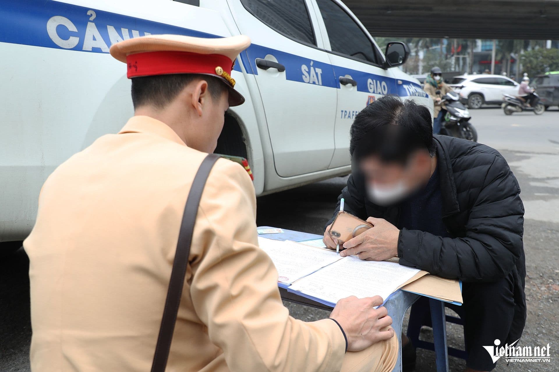 Cảnh sát giao thông đang lập biên bản xử phạt vi phạm giao thông cho người dân bên cạnh xe công vụ, minh họa sự nghiêm minh trong xử lý vi phạm.