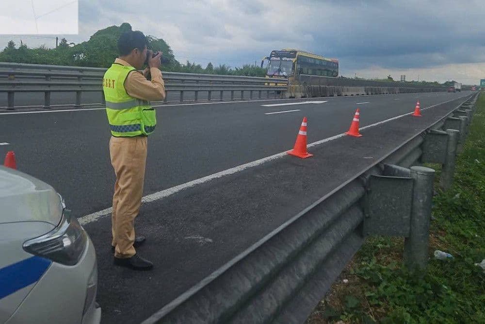 Cảnh sát giao thông 'áo vàng' đứng bên đường cao tốc, sử dụng thiết bị giám sát, thể hiện sự chuyển đổi từ tuần tra công khai sang phạt nguội.
