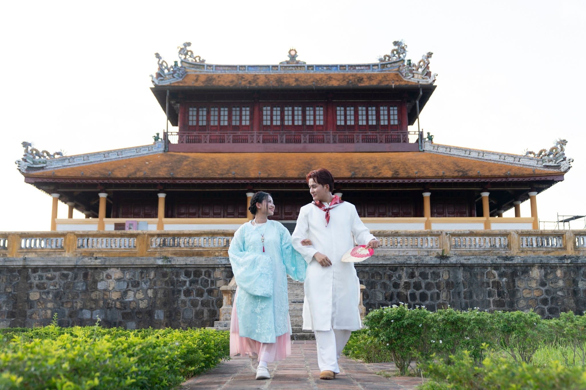 Cặp đôi mặc trang phục truyền thống Huế đi dạo trước kiến trúc cổ kính.