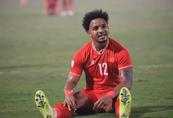 Cầu thủ bóng đá ngồi trên sân, thể hiện sự mệt mỏi hoặc thất vọng sau trận đấu