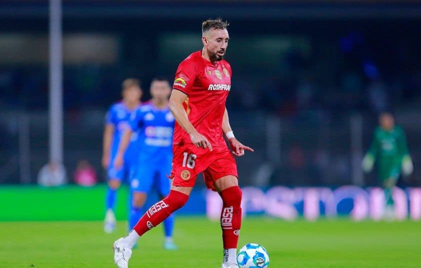 Cầu thủ bóng đá trong trang phục màu đỏ đang dẫn bóng trên sân cỏ, tượng trưng cho trận đấu giữa Atl. San Luis và Toluca.