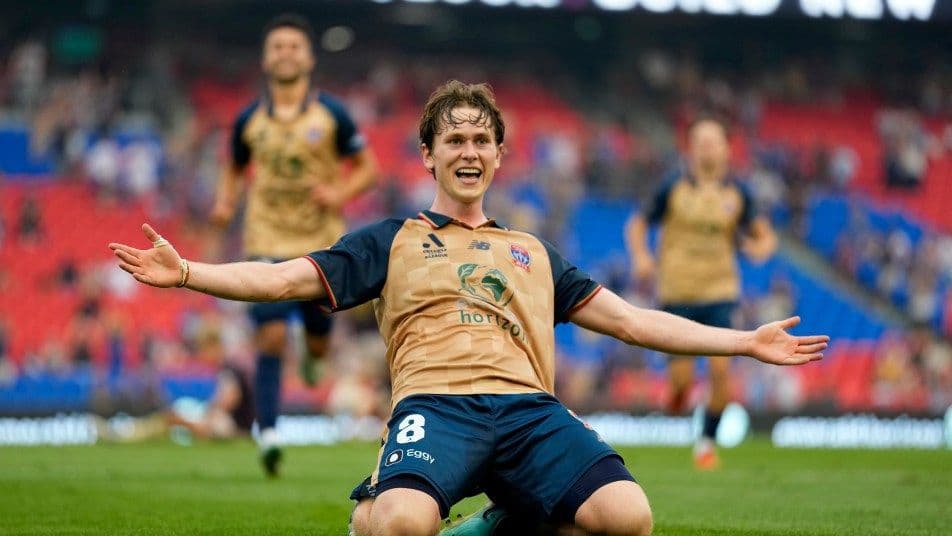 Cầu thủ Lachlan Bayliss của Newcastle Jets ăn mừng bàn thắng với vòng tay rộng mở trên sân cỏ, thể hiện niềm vui chiến thắng trong A-League.