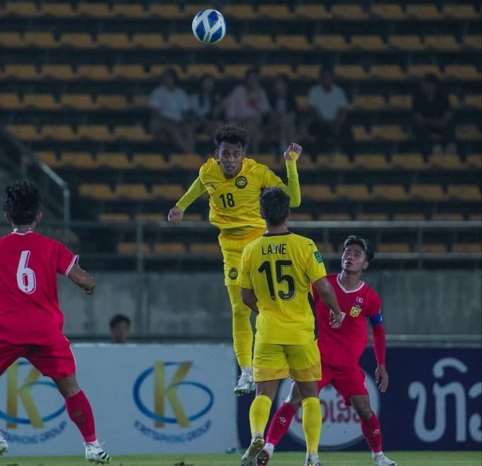 Cầu thủ Malaysia (áo vàng) tranh chấp bóng với cầu thủ Lào (áo đỏ) trong trận đấu vòng loại Asian Cup 2027, thể hiện chiến thắng nhưng đầy áp lực.