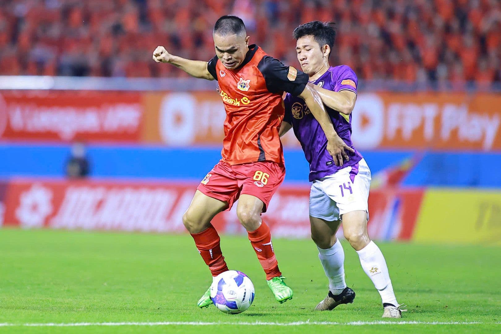 Cầu thủ Ninh Bình FC (áo đỏ) trong pha tranh chấp bóng với cầu thủ Hà Nội FC, minh họa lối chơi trực diện bị Văn Quyết chỉ trích.