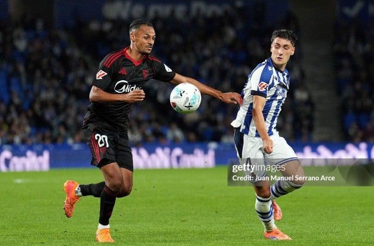 Cầu thủ Sevilla (áo đen) và Real Sociedad (áo sọc xanh trắng) tranh chấp bóng trên sân cỏ.
