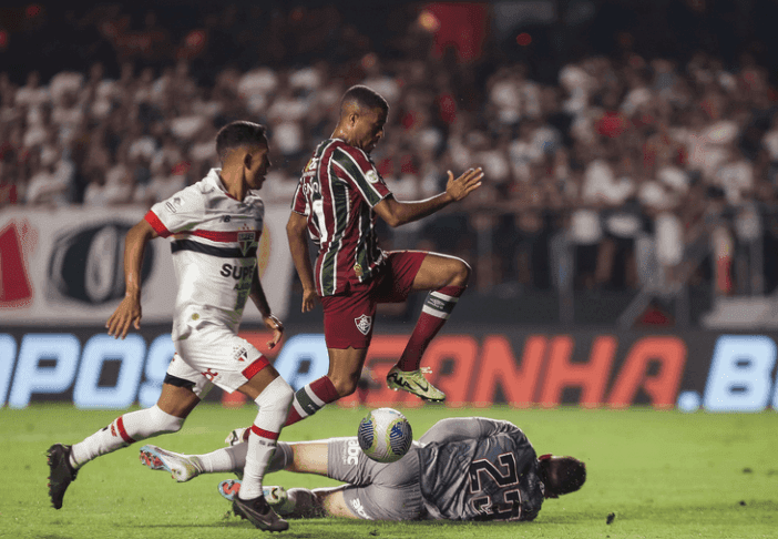 Cầu thủ tấn công vượt qua thủ môn, thể hiện nỗ lực tìm kiếm bàn thắng.