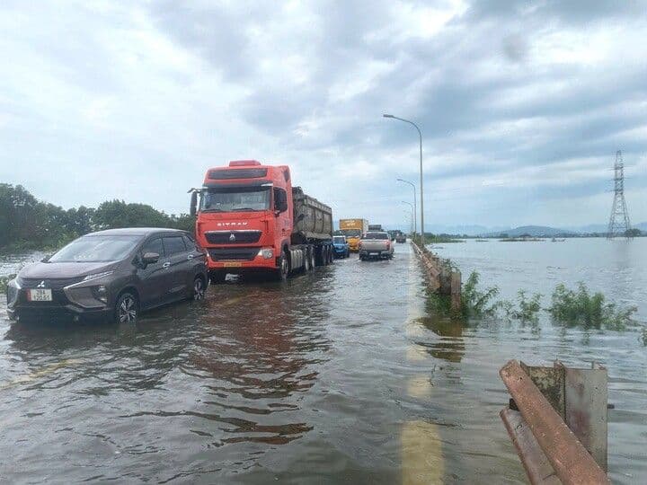 Dòng xe tải và ô tô con di chuyển chậm chạp trên tuyến đường đô thị ngập nước, thể hiện tình trạng quá tải và thách thức giao thông