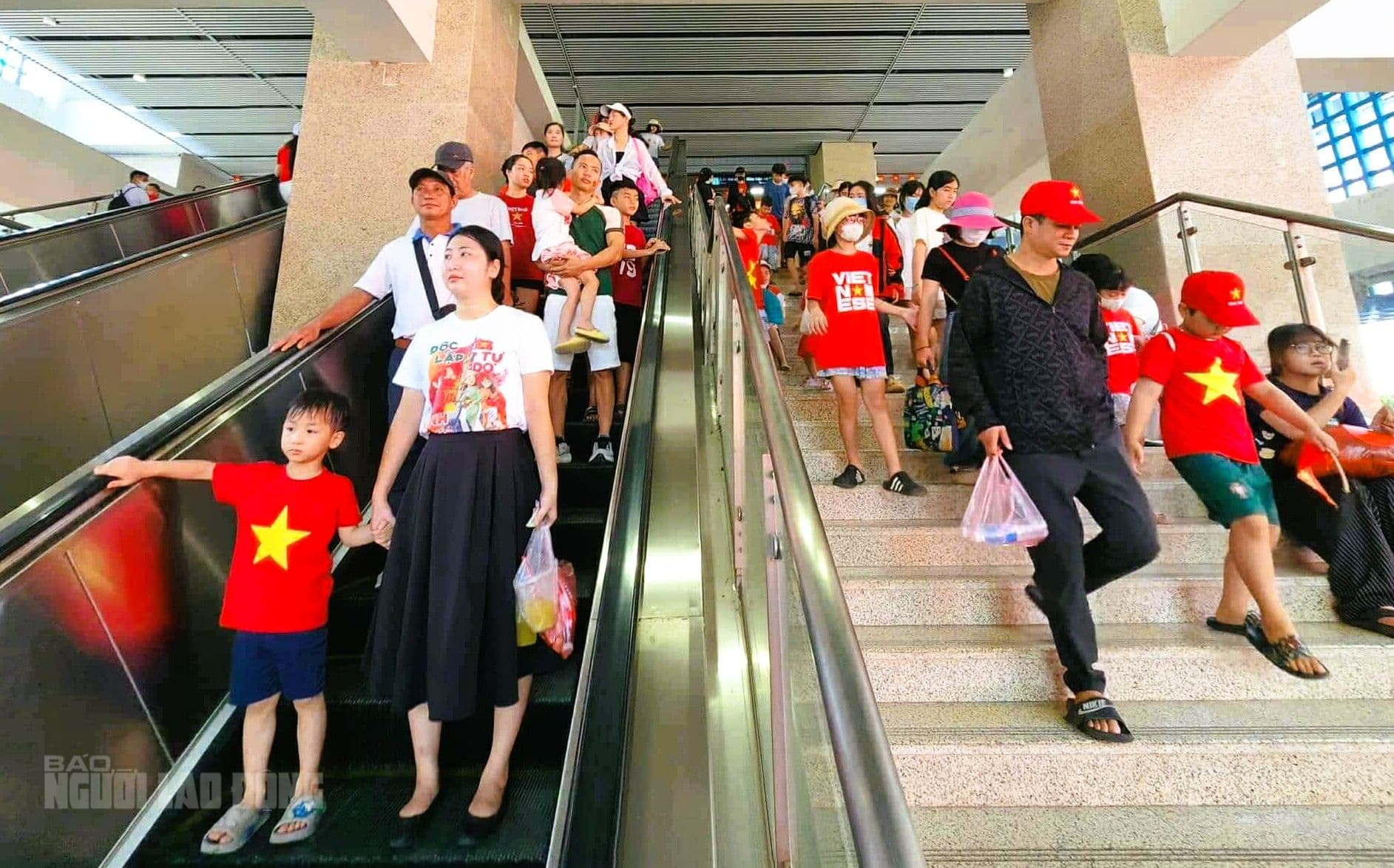 Gia đình và trẻ em mặc áo cờ đỏ sao vàng di chuyển bằng thang cuốn tại ga metro.