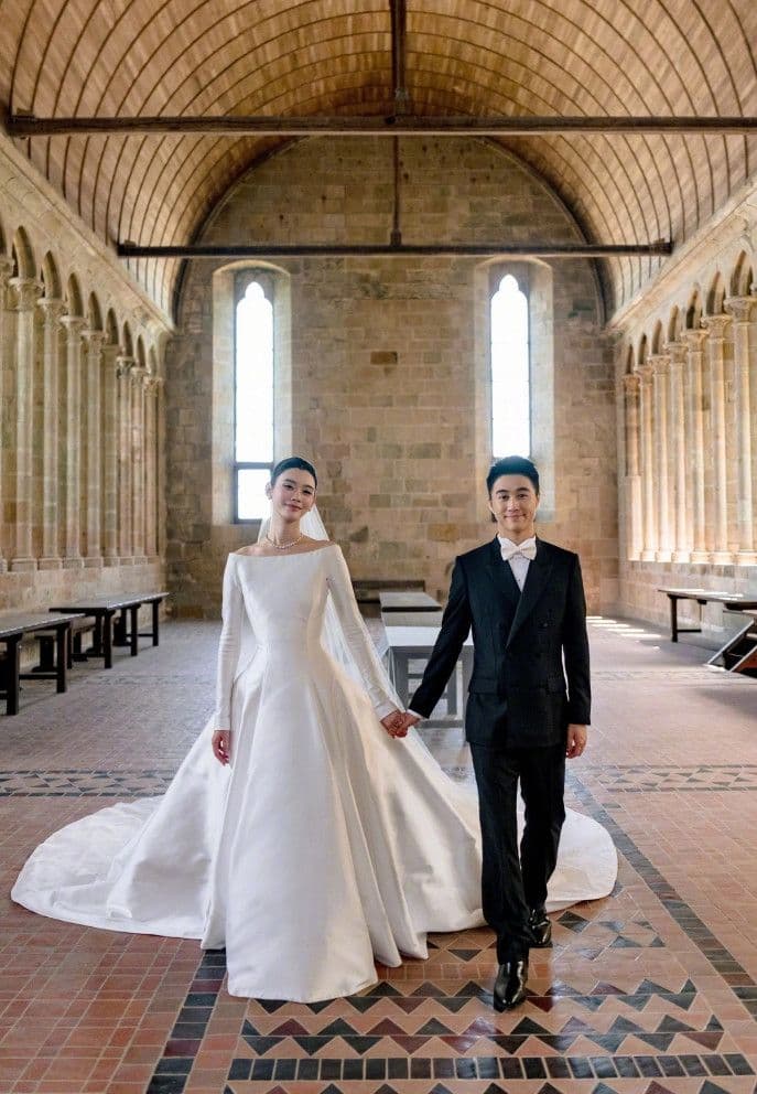 Hề Mộng Dao và Hà Du Quân nắm tay nhau bước đi trong lễ đường cổ kính, tượng trưng cho hôn lễ hiện đại.