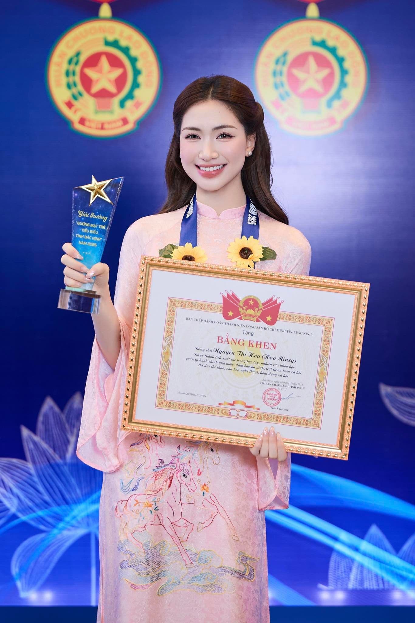 Hòa Minzy rạng rỡ trong áo dài hồng, cầm giải thưởng và bằng khen, tượng trưng cho đỉnh cao sự nghiệp của cô.