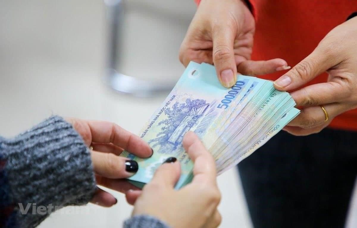 Hai bàn tay đang trao đổi tiền Việt Nam, tượng trưng cho việc chi trả lương và mức lương tối thiểu.