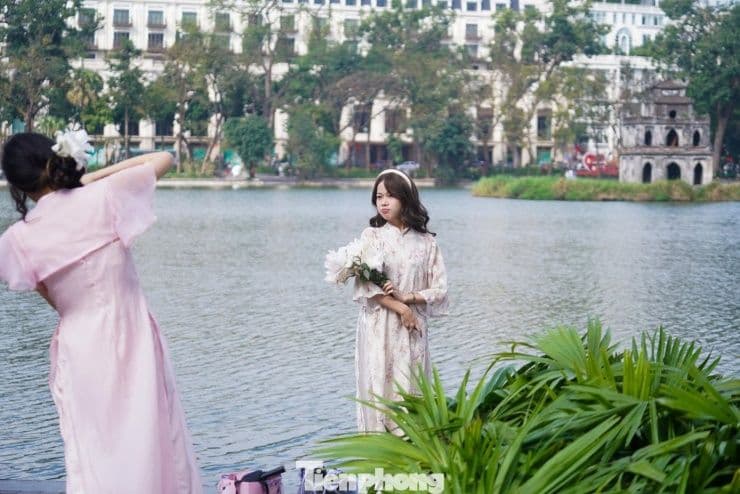 Hai cô gái mặc áo dài truyền thống chụp ảnh bên Hồ Gươm trong thời tiết đẹp, nắng nhẹ ở miền Bắc.