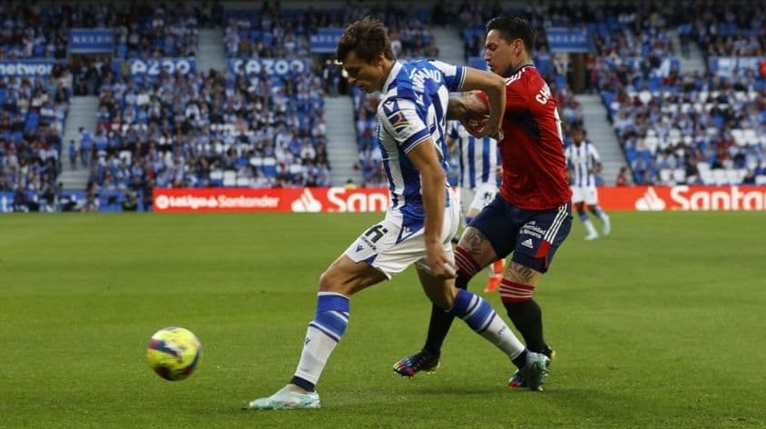 Hai cầu thủ Real Sociedad và Osasuna tranh bóng quyết liệt trên sân cỏ, thể hiện sự đối đầu trong trận đấu La Liga.