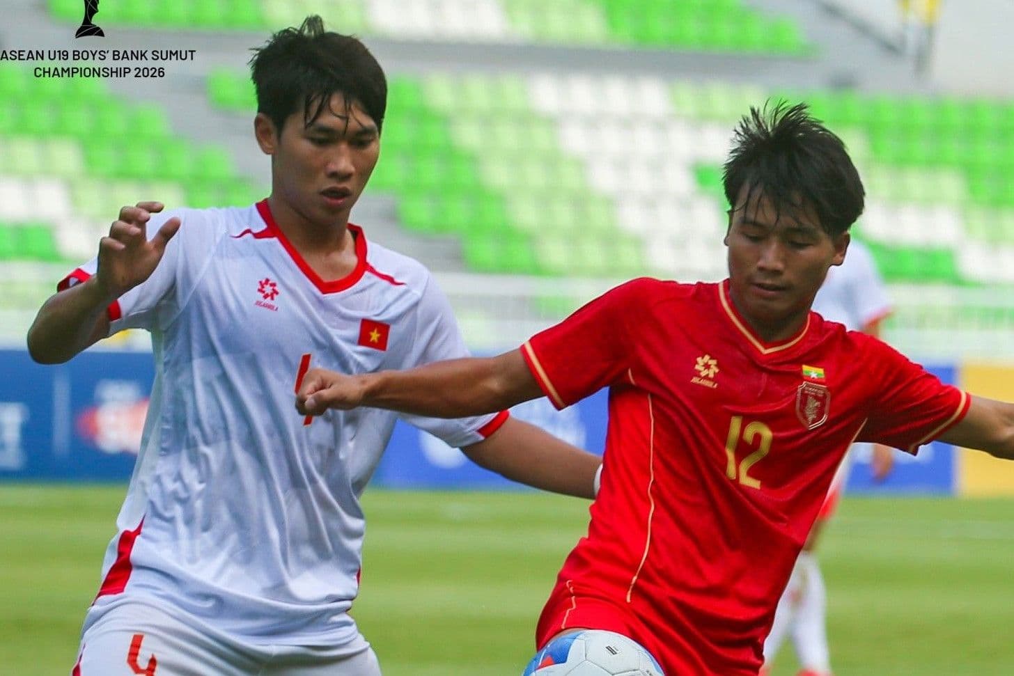 Hai cầu thủ U19 Việt Nam trong trang phục thi đấu trắng và đỏ tranh chấp bóng trên sân.