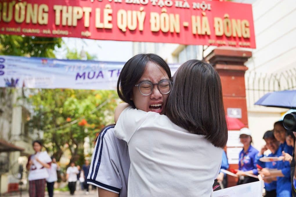 Hai nữ sinh ôm nhau, một người bật khóc sau kỳ thi tuyển sinh lớp 10 môn Toán tại Hà Nội, thể hiện áp lực và cảm xúc của thí sinh.
