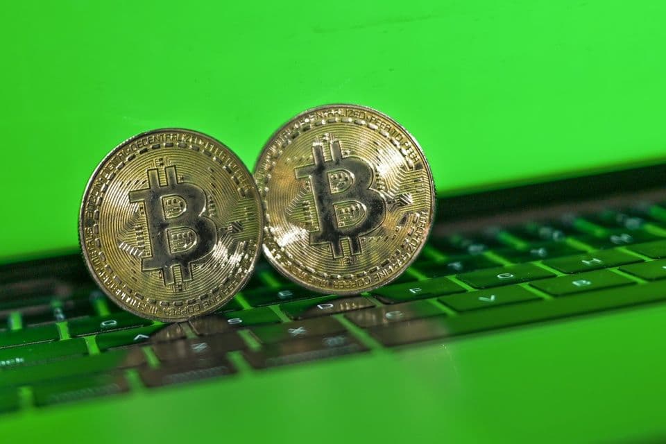 Hai đồng Bitcoin vật lý trên nền bàn phím màu xanh lá cây, tượng trưng cho tiền kỹ thuật số.