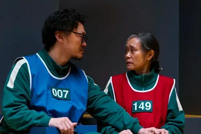 Hai người chơi Trò Chơi Con Mực trong trang phục xanh lá, thể hiện khía cạnh nhân văn và sự lựa chọn của con người trong trò chơi sinh tồn.