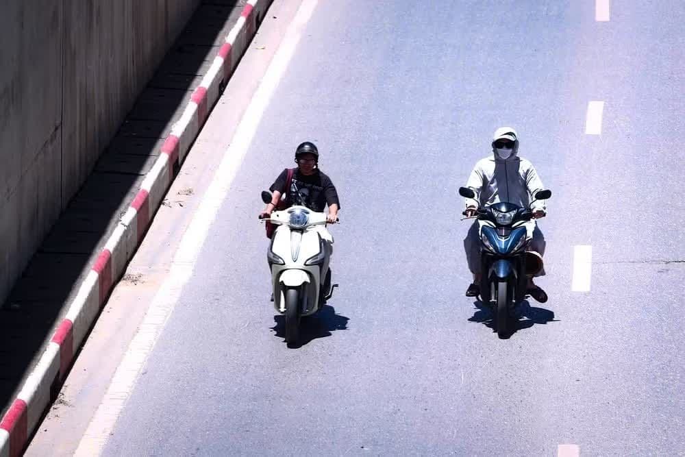 Hai người đi xe máy trên đường phố Hà Nội dưới trời nắng, thể hiện cuộc sống đô thị gắn liền với xe máy.
