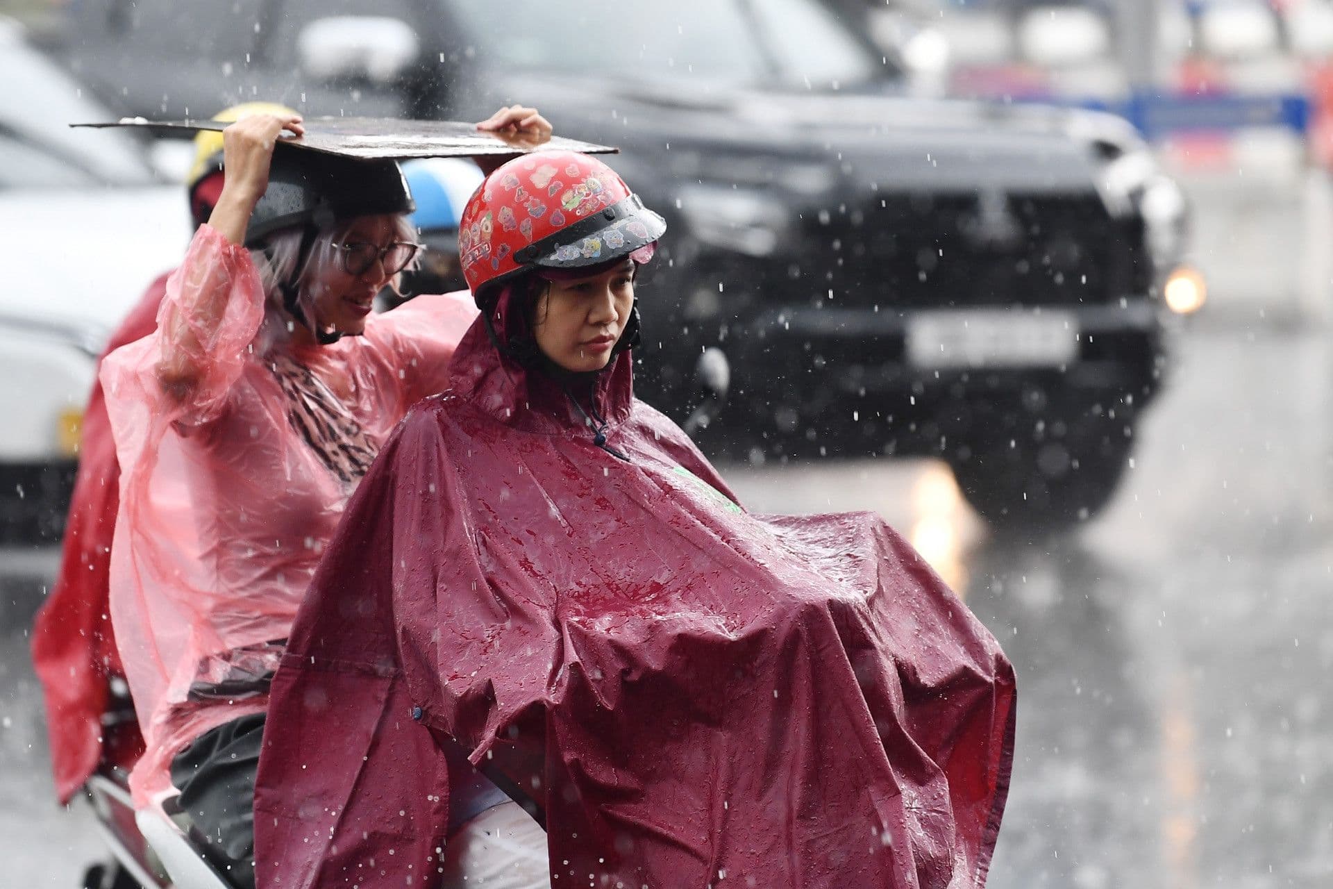 Hai người đi xe máy trong cơn mưa, minh họa cảnh báo giông lốc mạnh sau nắng nóng ở miền Bắc, dấu hiệu của biến đổi khí hậu.