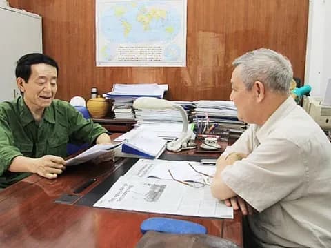 Hai người đàn ông thảo luận trong văn phòng, tượng trưng cho việc hoạch định chính sách hỗ trợ cộng đồng đón Tết theo Nghị quyết 48.