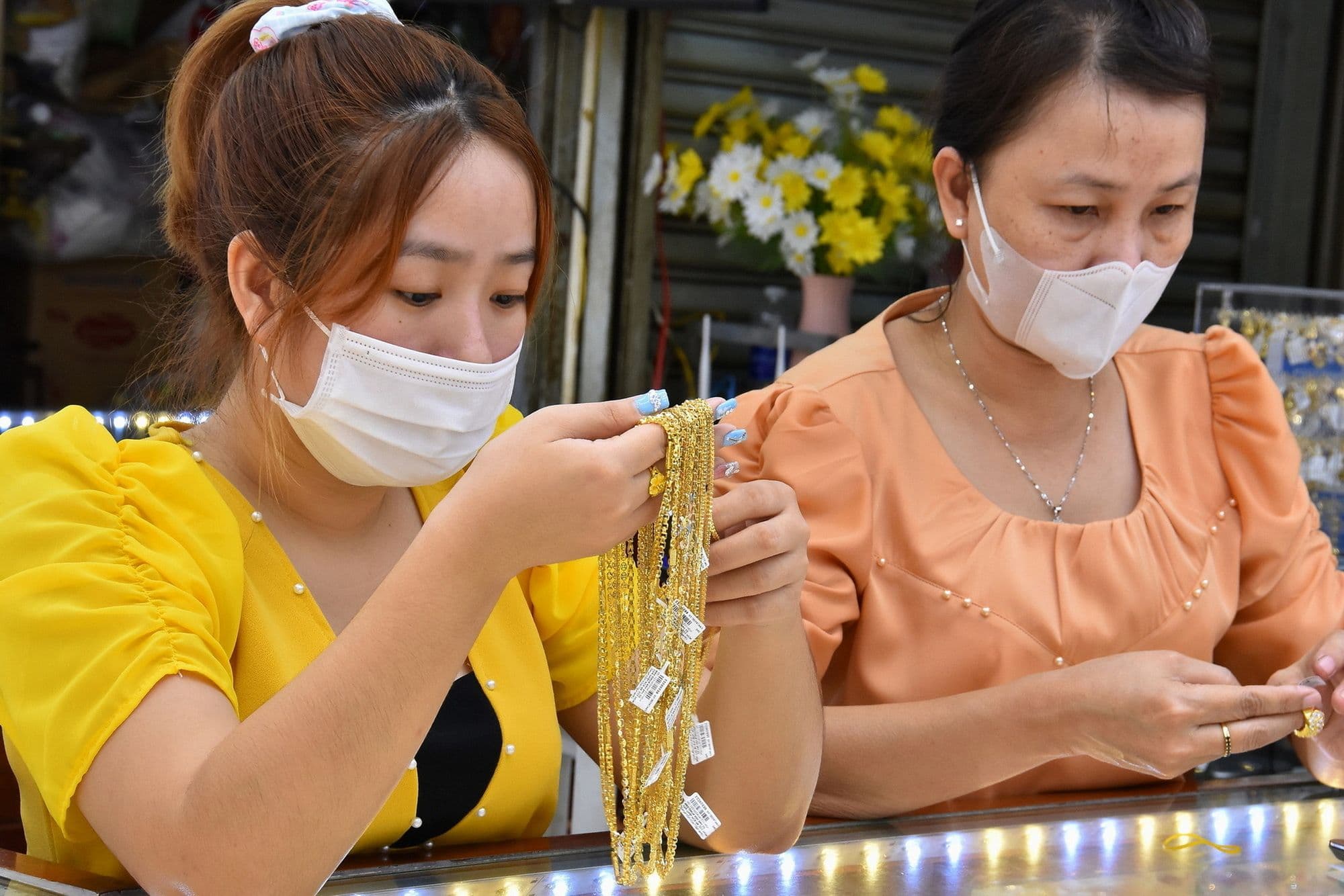Hai người phụ nữ đeo khẩu trang đang xem xét vàng tại một cửa hàng, phản ánh biến động thị trường vàng trong nước.