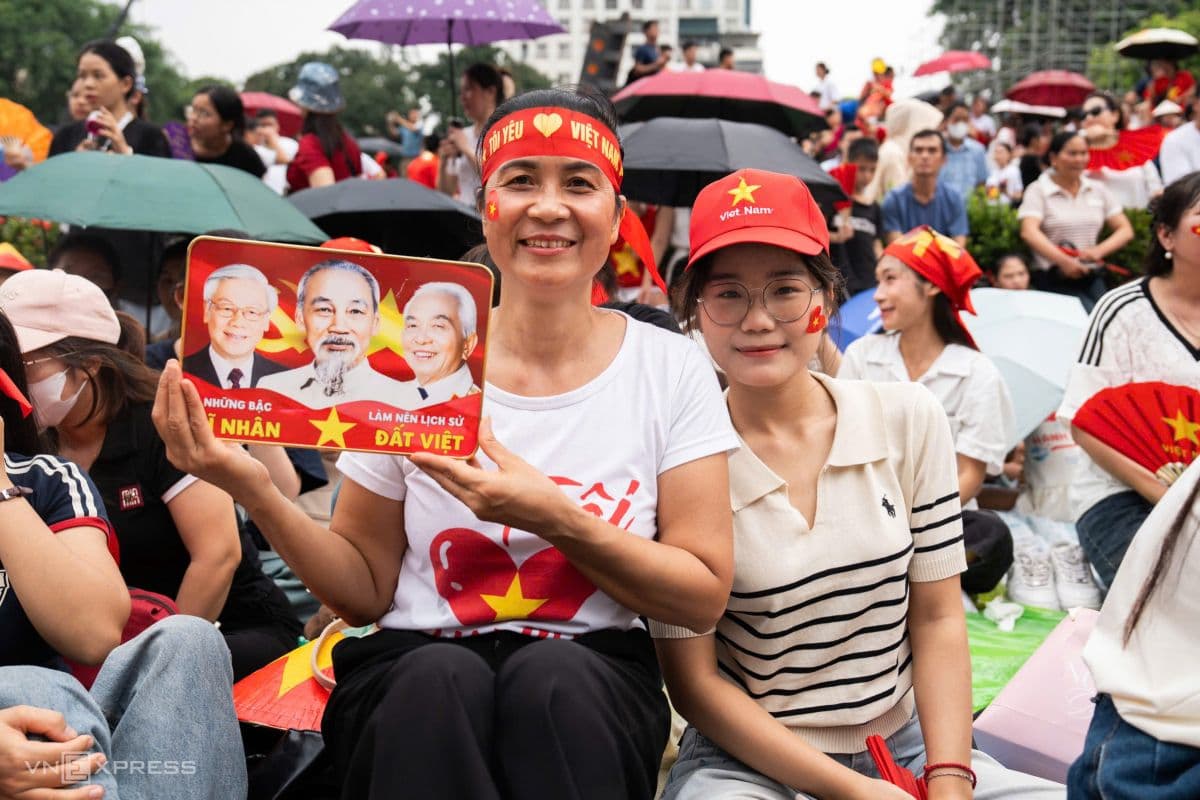 Hai người phụ nữ Hà Nội mặc áo cờ đỏ sao vàng, một người cầm biển hình các lãnh tụ, thể hiện niềm tự hào dân tộc.