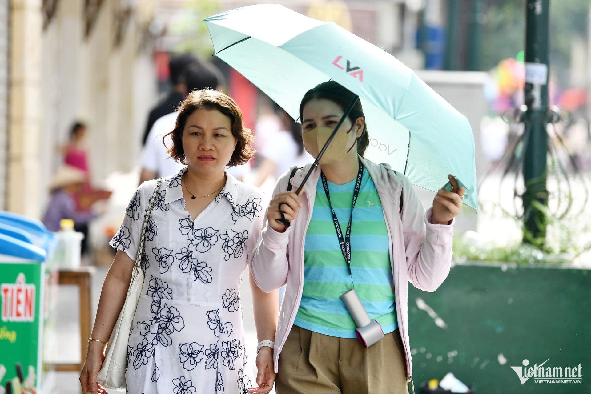Hai người phụ nữ đi bộ dưới nắng gắt, một người dùng ô che nắng, minh họa sự chuyển mình đột ngột của thời tiết giao mùa.