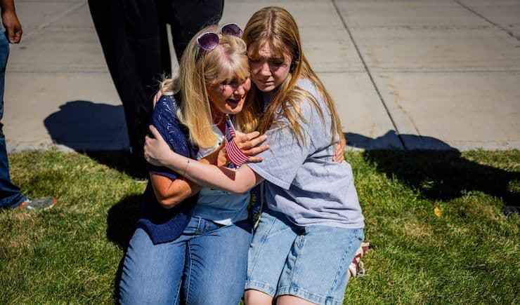 Hai người phụ nữ ôm nhau an ủi, một người cầm cờ Mỹ, sau vụ ám sát.